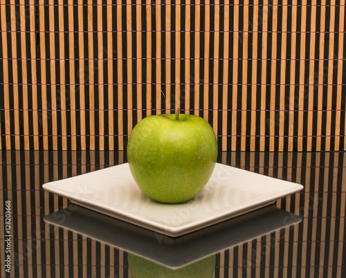 Green apple.Italy,November 20,2016,green apple on a white platter,composition on the table with a glass surface,the background texture of a bamboo. photo