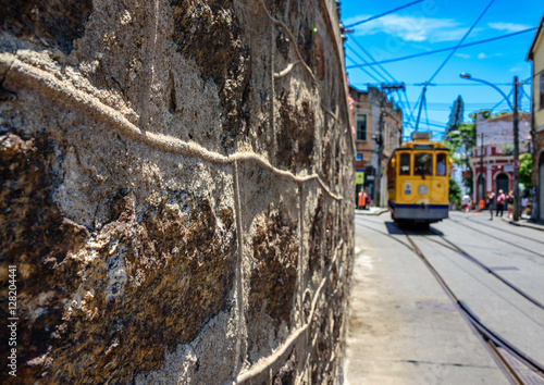 The stone wall, blue sky and old-fashioned yellow tram bonde going by tram tracks in Santa Teresa district of Rio de Janeiro, Brazil photo