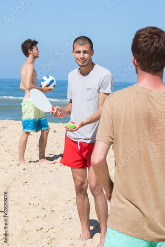 cheerful happy friends relaxing at beach and playing with rackets photo