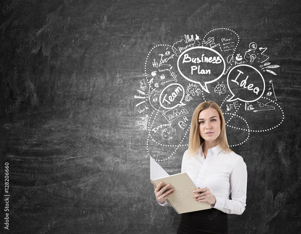 Blond woman with a notebook near a chalkboard with business plan Blond woman with a notebook near a chalkboard with business plan