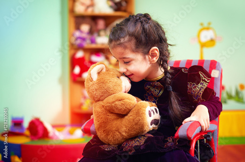 cute little girl in wheelchair hugging plush bear in kindergarte photo