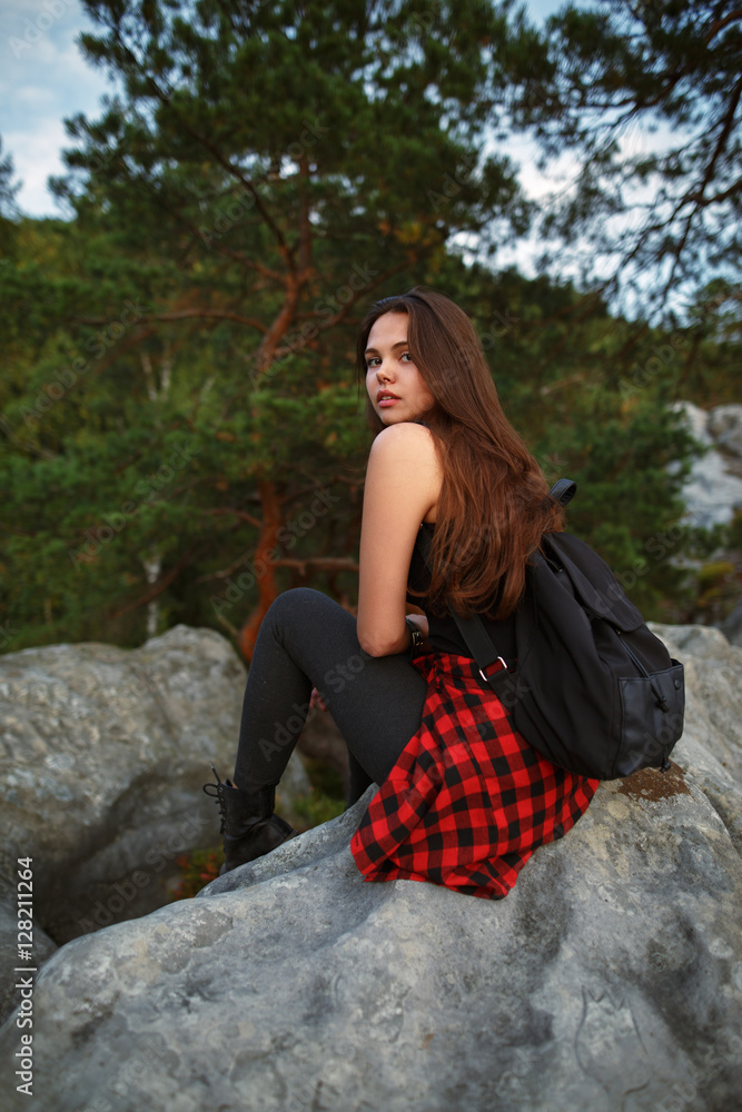 Young tourist with backpack relaxing on rock and enjoying sunset Young tourist with backpack relaxing on rock and enjoying sunset