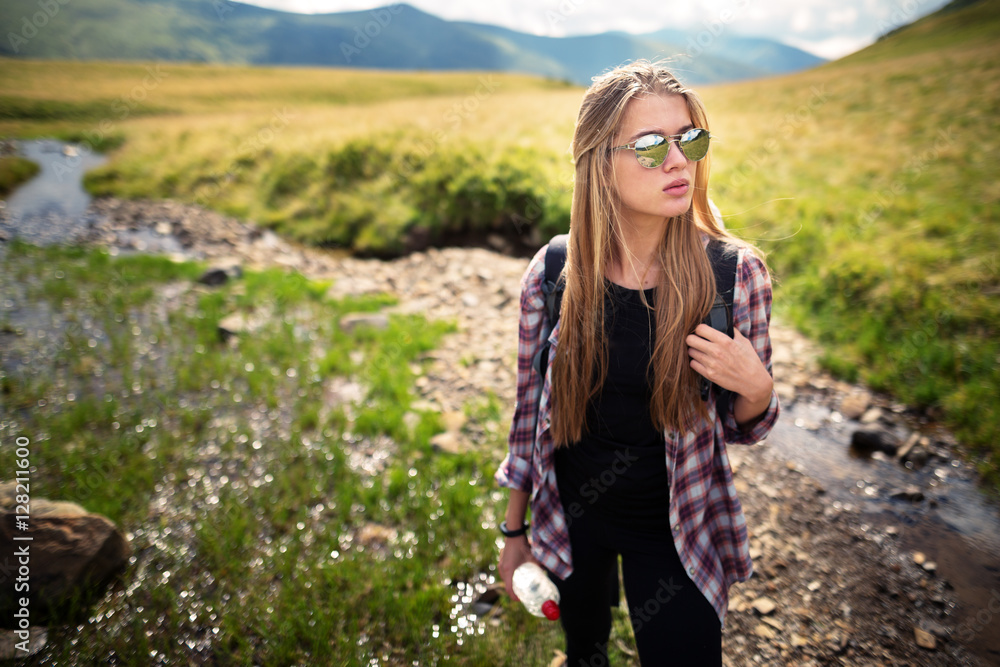 Outdoor shot of attractive young woman with backpack standing in a mountain stream. Female hiker in creek water.Portrait of young pretty woman holding bottle of water.