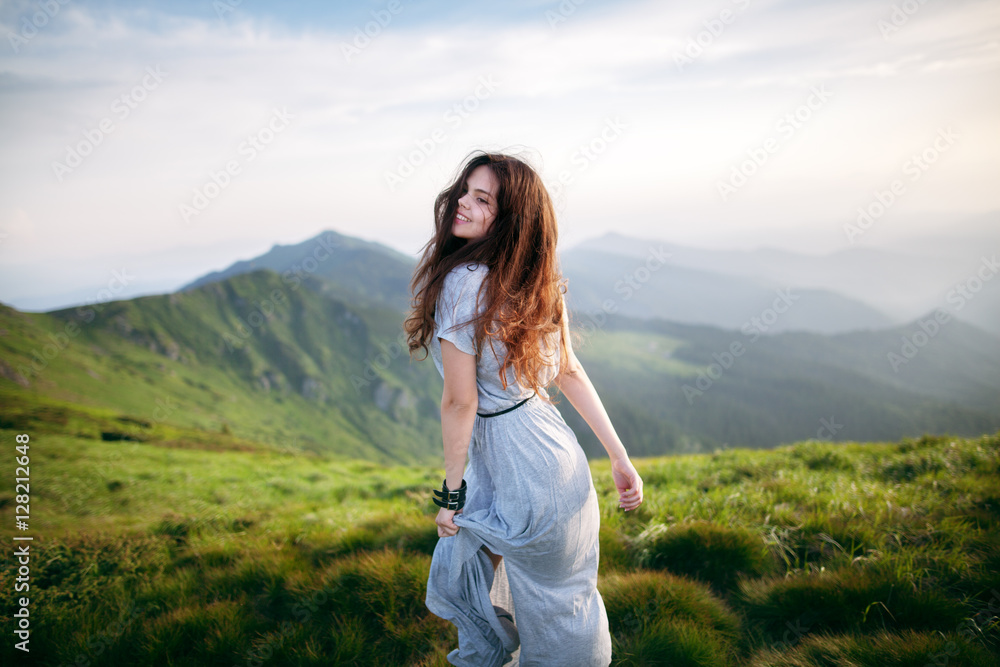 Young happy woman in long dress on the mountainside. Young girl in the mountains. Out of focus Young happy woman in long dress on the mountainside. Young girl in the mountains. Out of focus