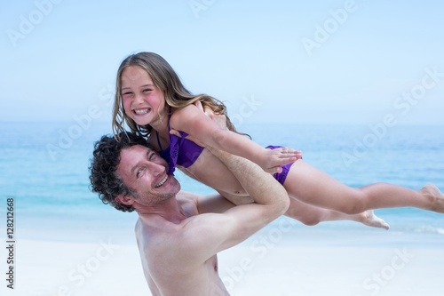 Cheerful shirtless man lifting daughter at sea shore photo