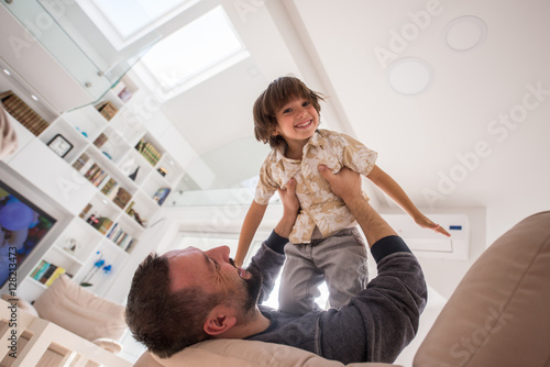 Cheerful young boy having fun with father on sofa
