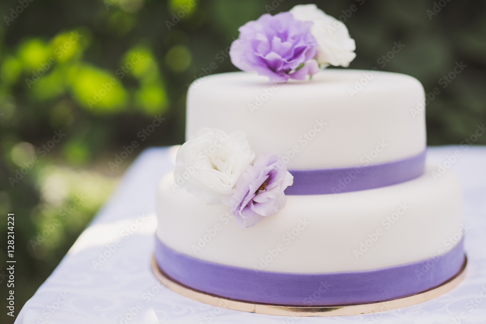 White wedding cake with purple decoration outdoors on the table White wedding cake with purple decoration outdoors on the table