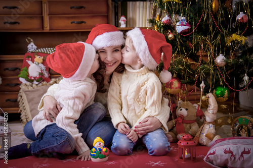 Kids kissing theit mother at cheek under Christmas tree photo