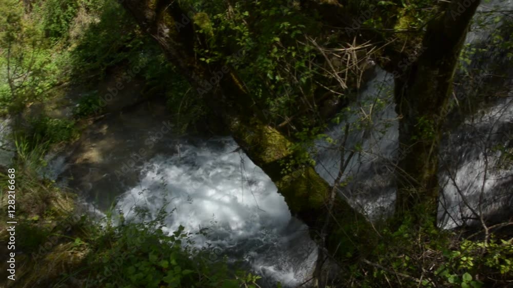 Hand-held camera shot of waterfall and river flow in a forest, where camera tilts down the waterfall and pans to the left following the stream of the river Hand-held camera shot of waterfall and river flow in a forest, where camera tilts down the waterfall and pans to the left following the stream of the river