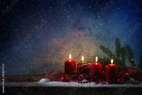 Four red advent candles burning in the snow against a blue vintage background, generous copy space
