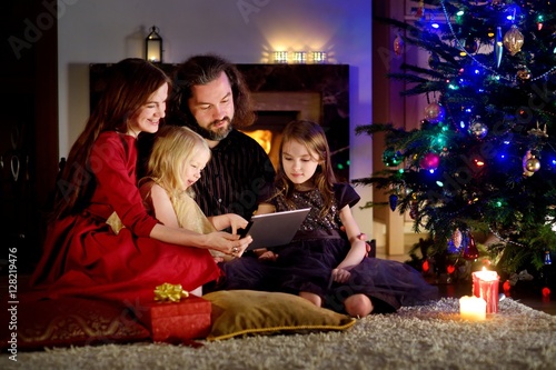 Happy young family using a tablet pc at home by a fireplace in warm and cozy living room © MNStudio