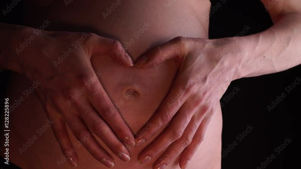 Woman no face making heart shape on the pregnant naked belly with hands, closeup on black. Concept of pregnancy, expecting a baby, love, parenthood. 4K ProRes HQ codec Woman no face making heart shape on the pregnant naked belly with hands, closeup on black. Concept of pregnancy, expecting a baby, love, parenthood. 4K ProRes HQ codec