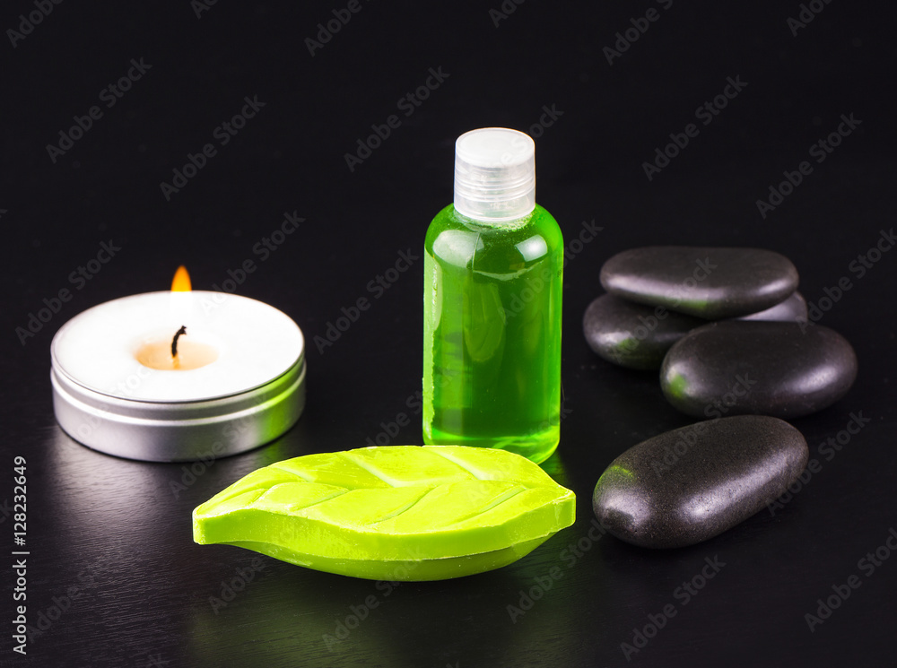 Soap, candle, bottle of oil and spa stones on black table.