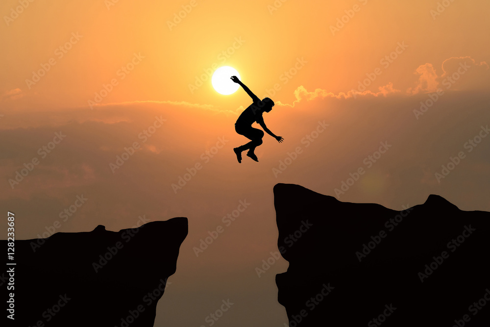 Man jump through the gap between hill.man jumping over cliff on sunset background,Business concept idea