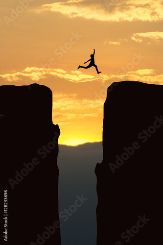 Man jump through the gap between hill.man jumping over cliff on sunset background,Business concept idea
