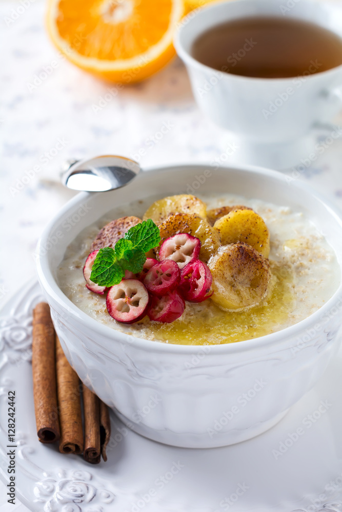Oat porridge with baked bananas, cinnamon,orange and cranberries in a ceramic bowl for healthy breakfast on a light background. Selective focus. Oat porridge with baked bananas, cinnamon,orange and cranberries in a ceramic bowl for healthy breakfast on a light background. Selective focus.