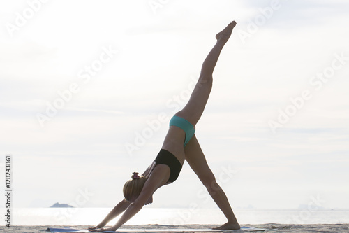 Young woman practices yoga on a beach at sunset
