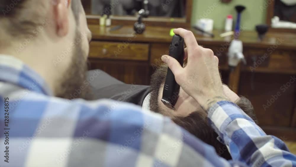 Barber woman trimming beard of client with clipper at barbershop Barber woman trimming beard of client with clipper at barbershop