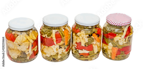 Jars with pickles containing cauliflower, cucumber, red pepper, onions, carrot, celery, isolated close up.