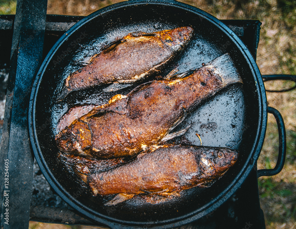 Cooking fresh fish fried BBQ with a delicious crispy golden crust in a cast- iron pan over an open fire outdoor Stock Photo