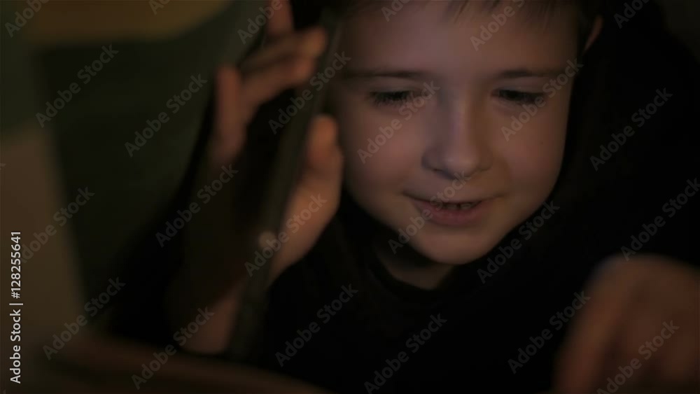 Boy reading book under covers and falls asleep at night. Close up. Little boy lying under covers