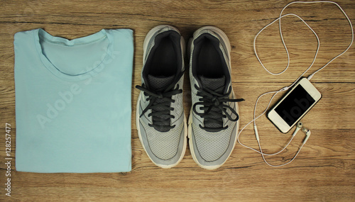 Set for sports: shoes, t-shirt, mobile phone with headphones close-up on a wooden background, top view