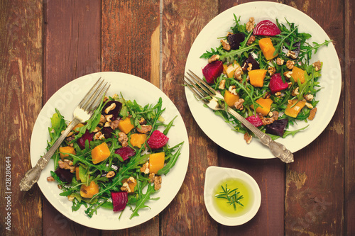 Fall salad with greens, arugula, walnuts, beetroot and roasted squash, pumpkin on wooden background