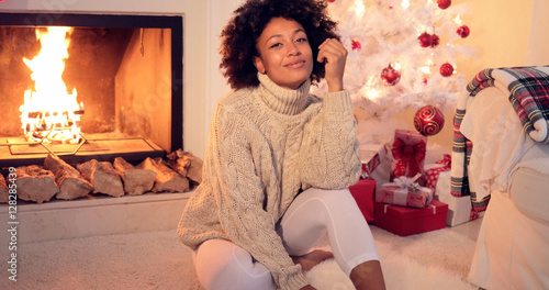 Woman by fireplace and white christmas tree covered in red ornaments and having many presents under it