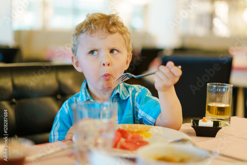 Foto Blond kid tries breakfast fruits with suspicious wary expression on his face