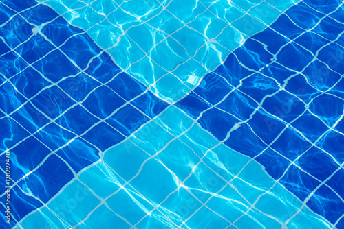 Bottom of the spa pool  lined with a checkered pattern of blue tiles  through the clear water  sparkling in the rays of sun.