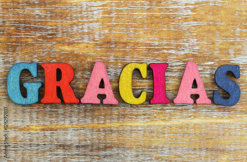 Gracias (thank you in Spanish) written with colorful letters on rustic wooden surface
