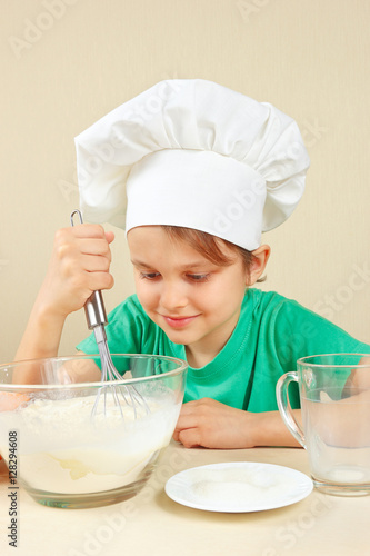 Little boy in chef hat shuffles dough for baking the cake