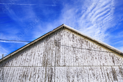 A low angle of the apex of a old barn with peeling paint with blue sky in the background