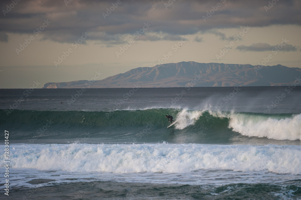Santa Cruz Island in background as surfer picks up speed across wind blown wave at dawn.