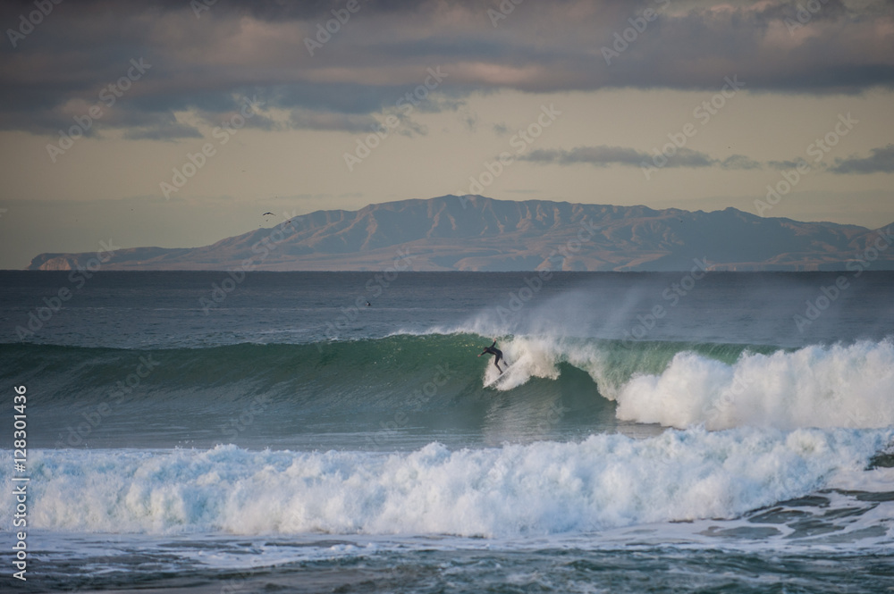 Santa Cruz Island in background as surfer drops into wind blown wave at dawn. Santa Cruz Island in background as surfer drops into wind blown wave at dawn.
