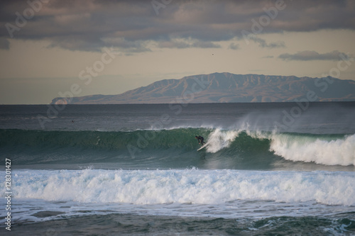 Santa Cruz Island in background as surfer picks up speed across wind blown wave at dawn.