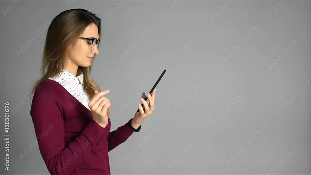 Beautiful young woman in glasses and business casual style using tablet on grey background with a copy space Beautiful young woman in glasses and business casual style using tablet on grey background with a copy space