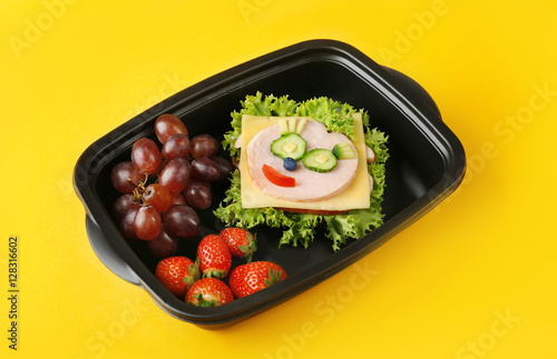 Tasty sandwich and fruits in lunchbox on yellow background