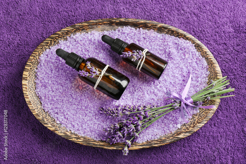 Bottles of essential oil and sea salt with lavender in wooden tray on towel background