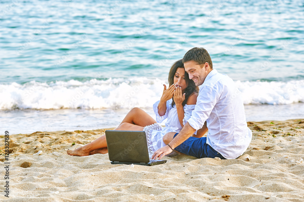 Beautiful romantic couple on the beach . Watching pictures on the laptop while traveling
