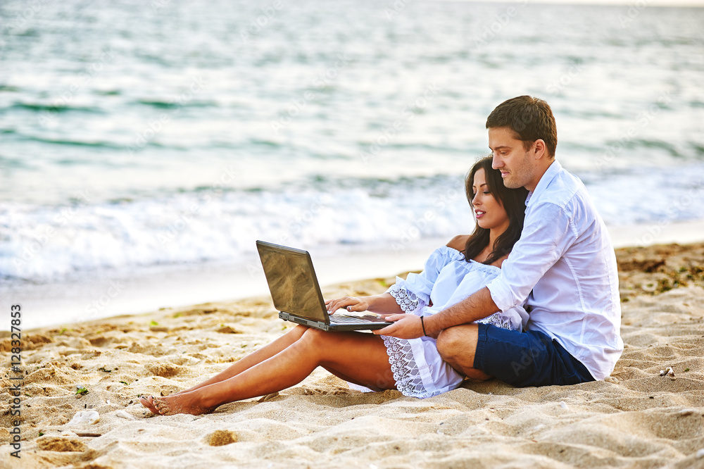 Beautiful romantic couple on the beach . Watching pictures on the laptop while traveling