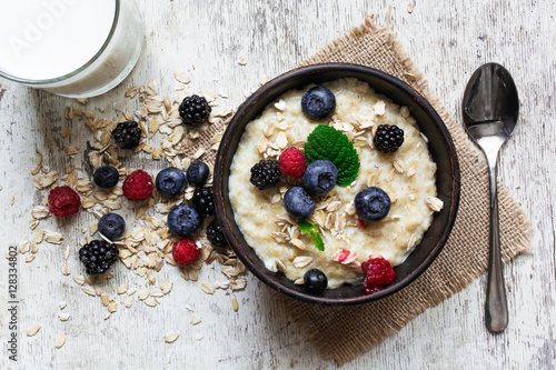 oatmeal porridge with fresh berries, glass of milk and spoon