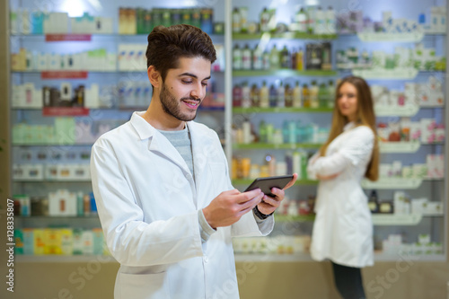 Portrait of pharmacist holding digital tablet in pharmacy,  in the background is a woman