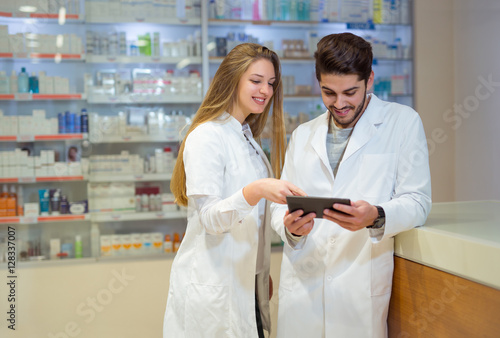 Pharmacists using digital tablet while checking medicine in pharmacy