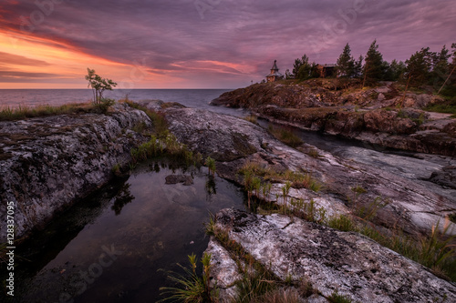 An island in the Ladoga lake with striped granite cliffs and small pond. Smooth surface of the pond reflects clouds lighted by a vivid sunrise. An orthodox church stands at cape of the island, Karelia photo