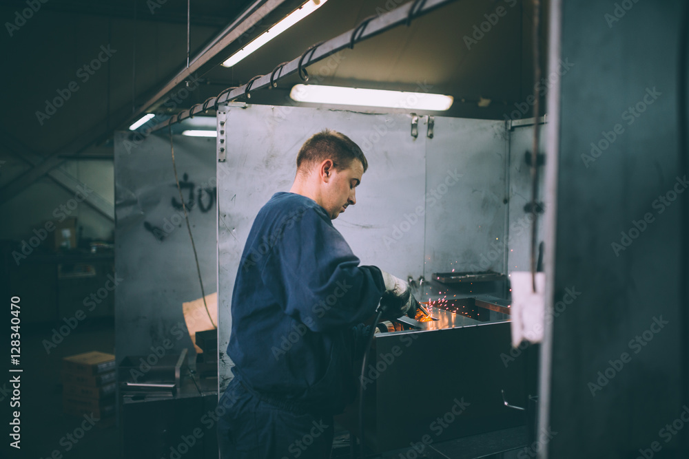 Metallurgy industry. Factory for production of heavy pellet stoves and boilers. Manual worker welder on his job. Extremely dark conditions and visible noise. Focus on foreground.