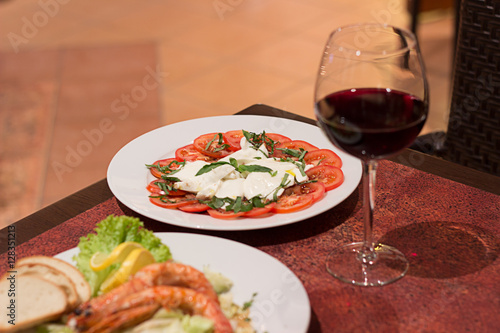 Restaurant food with fresh ingredients - tomatoes with mozzarella and fresh basil and glass of red wine