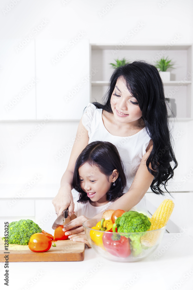 Cute girl cutting tomato with mother