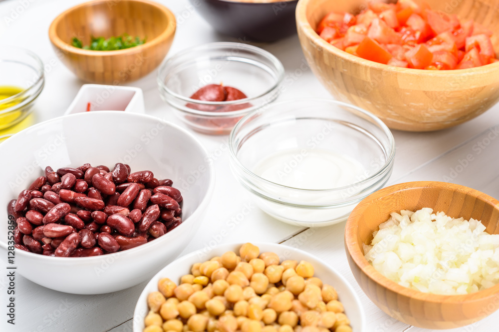 White And Red Kidney Beans, Ketchup, Tomatoes, Yogurt, Chickpeas, Garlic, And Onion Food Ingredients On White Wood Table White And Red Kidney Beans, Ketchup, Tomatoes, Yogurt, Chickpeas, Garlic, And Onion Food Ingredients On White Wood Table
