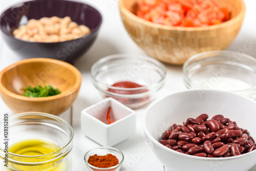 White And Red Kidney Beans, Chili Pepper, Parsley, Ketchup, Tomatoes, Olive Oil, Paprika And Yogurt Food Ingredients On White Wood Table